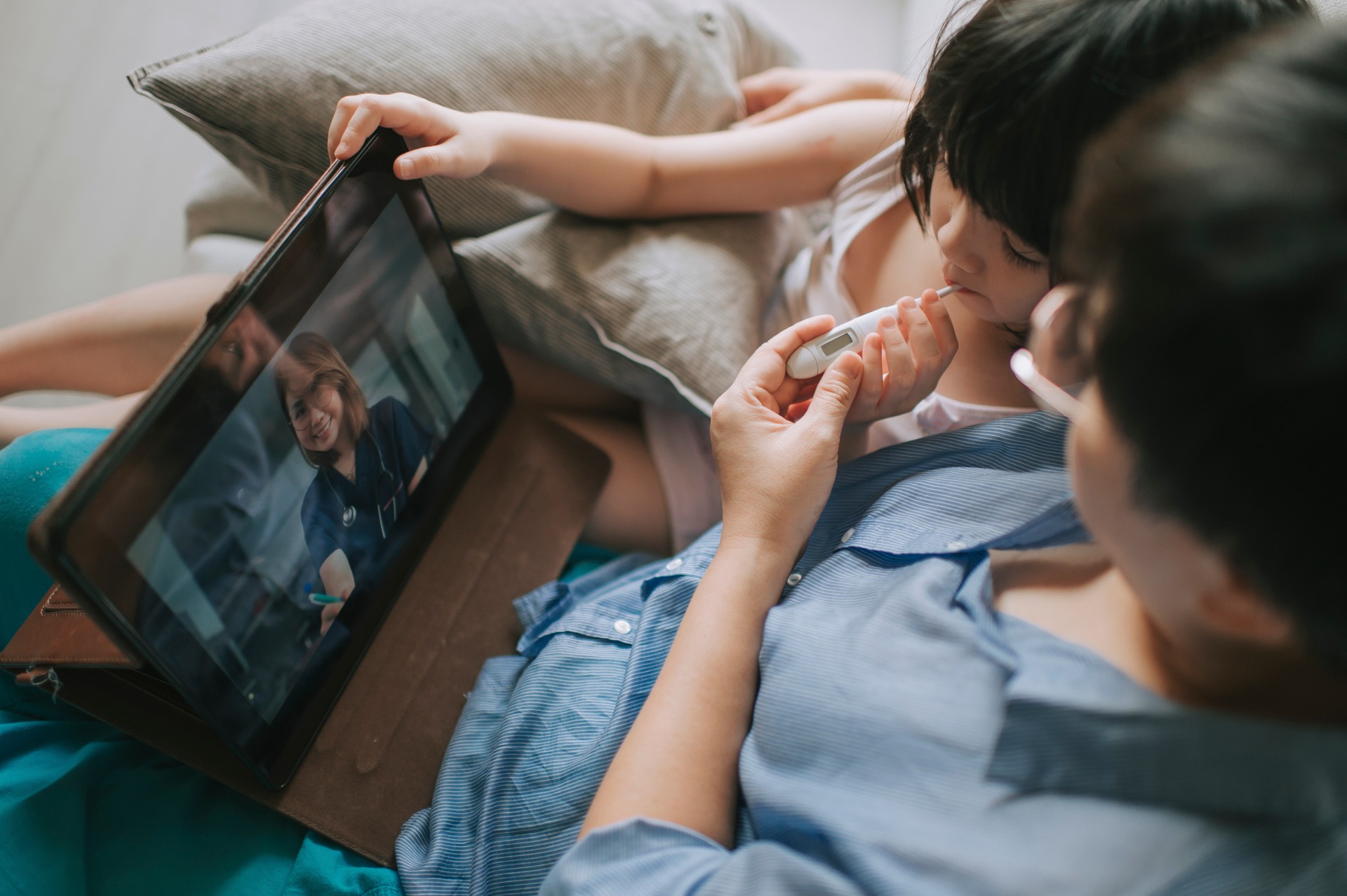 Telemedicine telehealth asian chinese mother using digital tablet communicate with doctor pediatrician on her daughter sickness after taking her daughter temperature